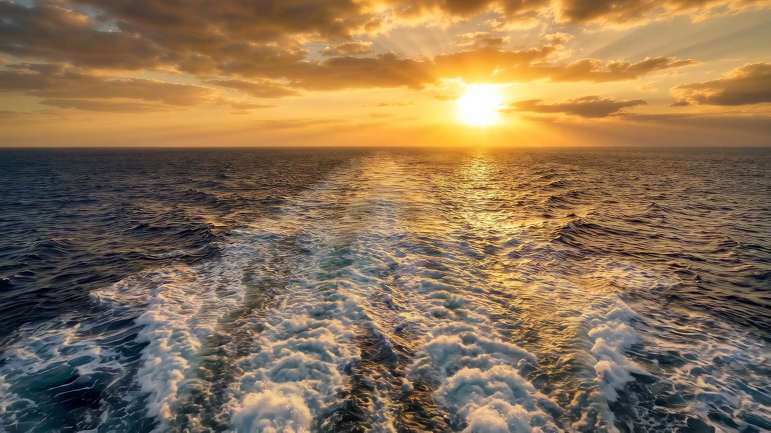 A cruise ship's wake stretching toward the sunset on the open ocean